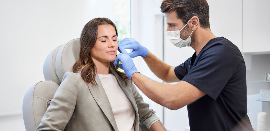 Eine braunhaarige Frau wird von einem Arzt mit Mundschutz behandelt.