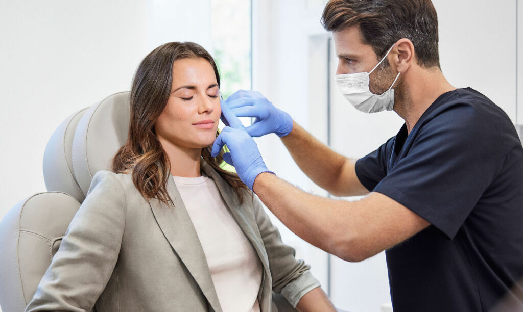 Eine braunhaarige Frau wird von einem Arzt mit Mundschutz behandelt.